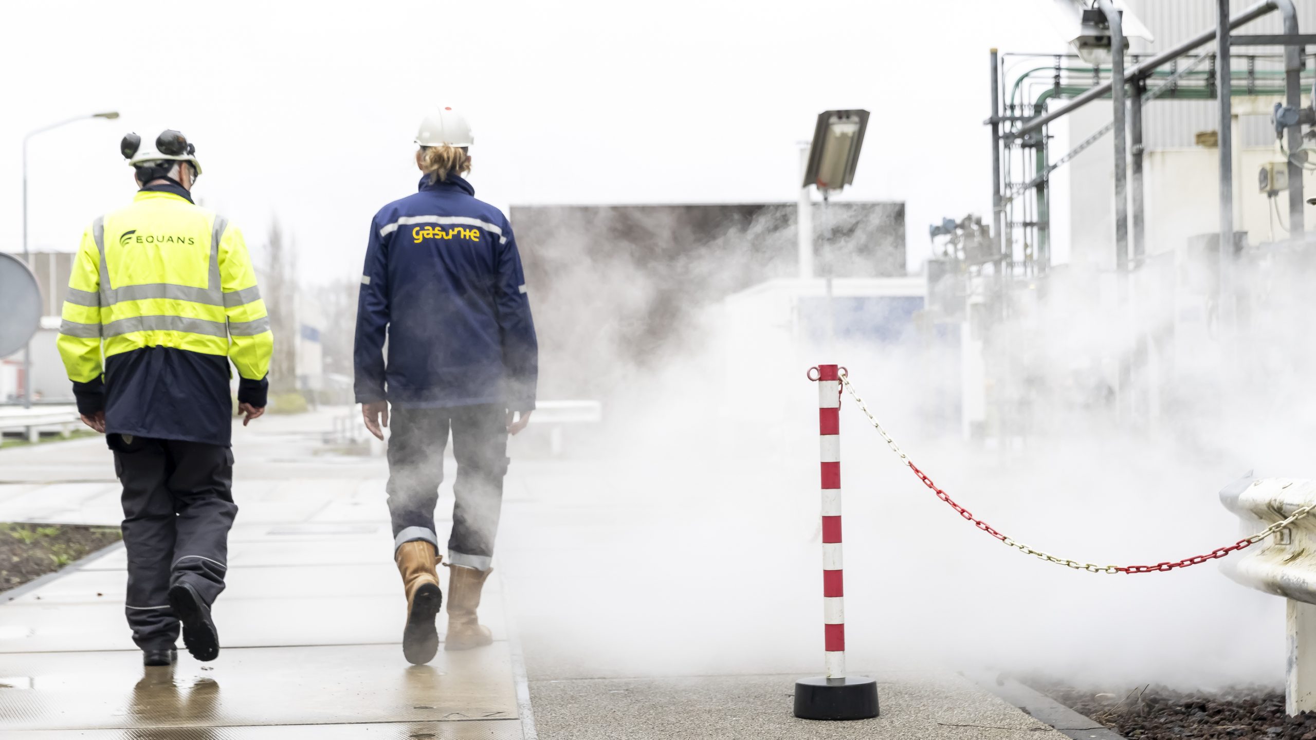 twee mannen lopen langs stoom op het terrein van gasunie